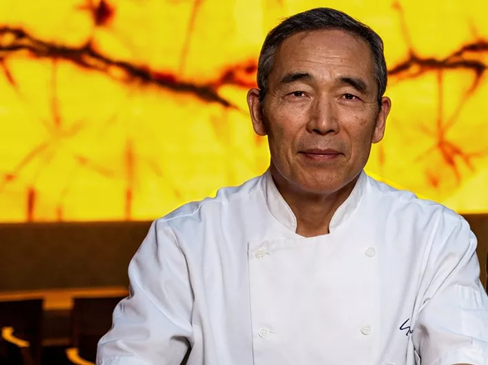 man in a chef coat in front of a yellow background