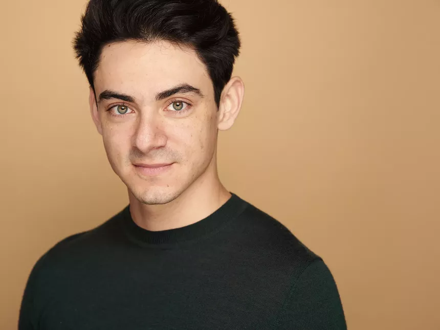 headshot of man with black hair wearing a black sweater