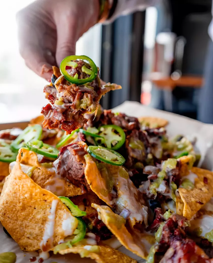 hand picking up a chip from a plate of nachos