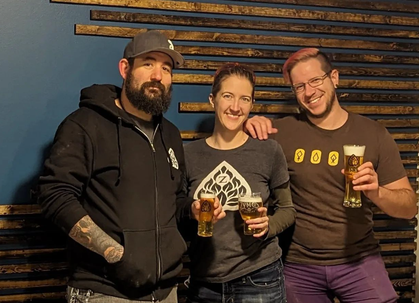 three people holding glasses of beer and posing