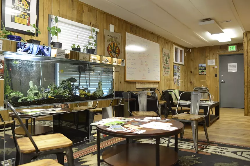 A fish tank inside of a marijauna dispensary waiting room with tables and chairs.
