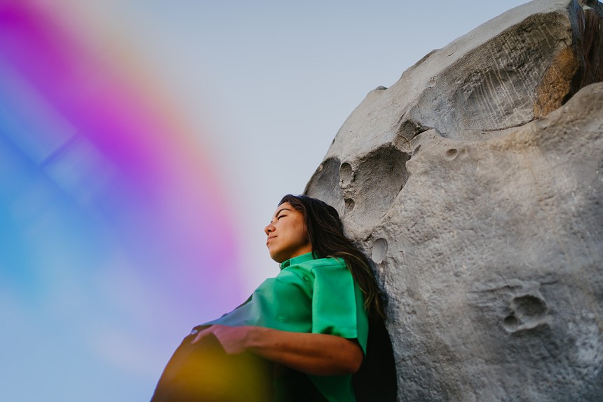 woman in green shirt leaning against a rock