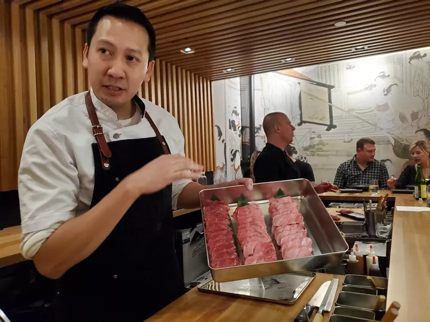a man in an apron holding a tray of sliced raw tuna