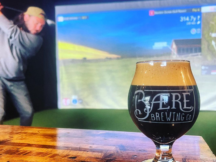 a glass of dark beer in front of a golf simulator