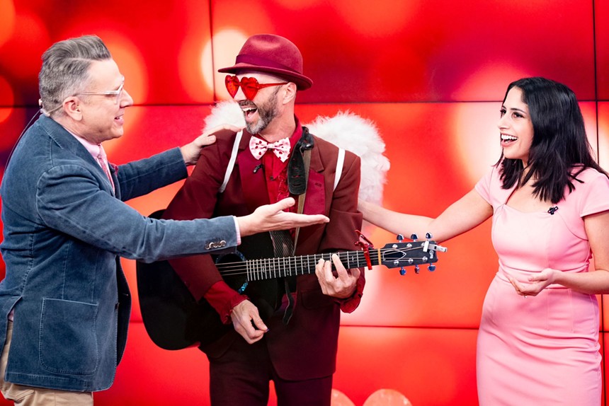 man in heart sunglasses and angel wings playing guitar to two people