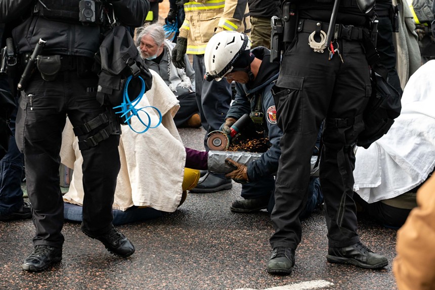 Police officer using a small circular saw to free pro-Palestine protesters.