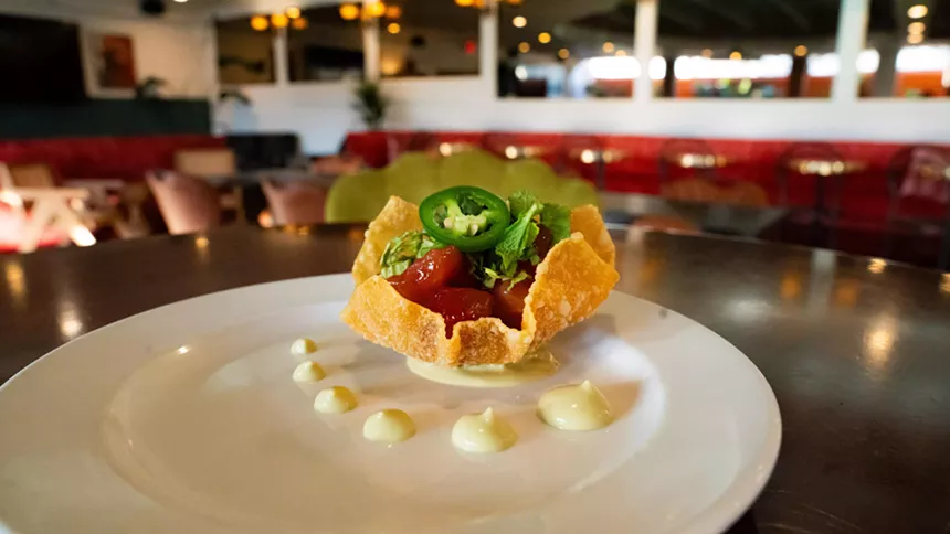 A tuna wonton on a white plate with lounge seating in the background