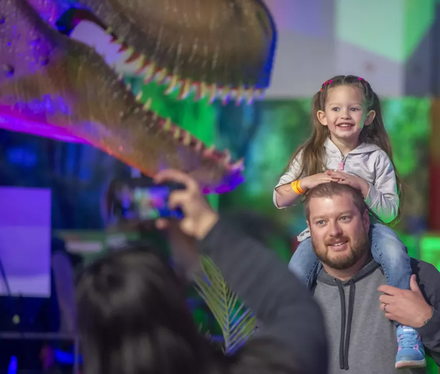 child on father's shoulders at dinosaur show