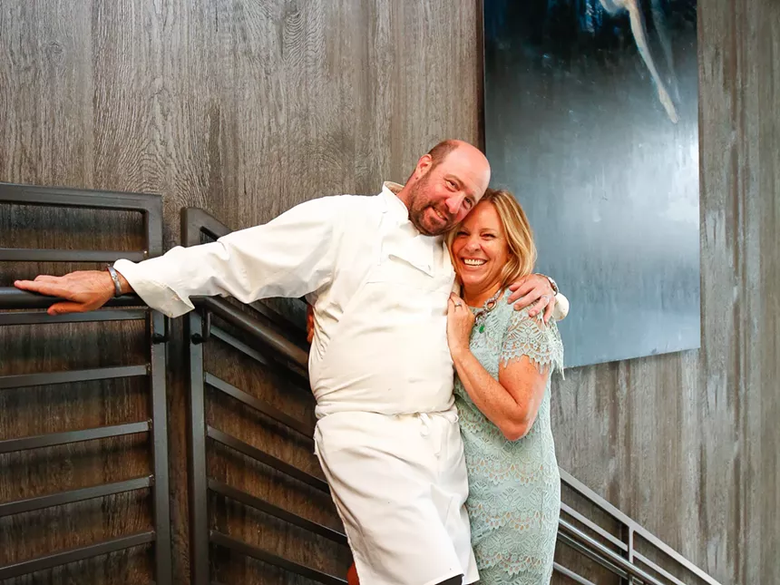 a man in a chef's coat and apron posing with a woman in a dress