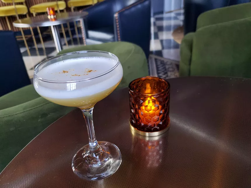 a cocktail in a coupe glass next to a glass votive candleholder