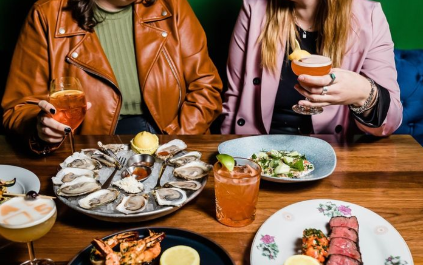 oysters one a plate in front of two women holding drinks