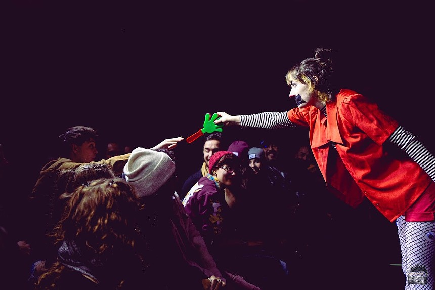 audience member reaching out to a woman with clown makeup holding a green toy