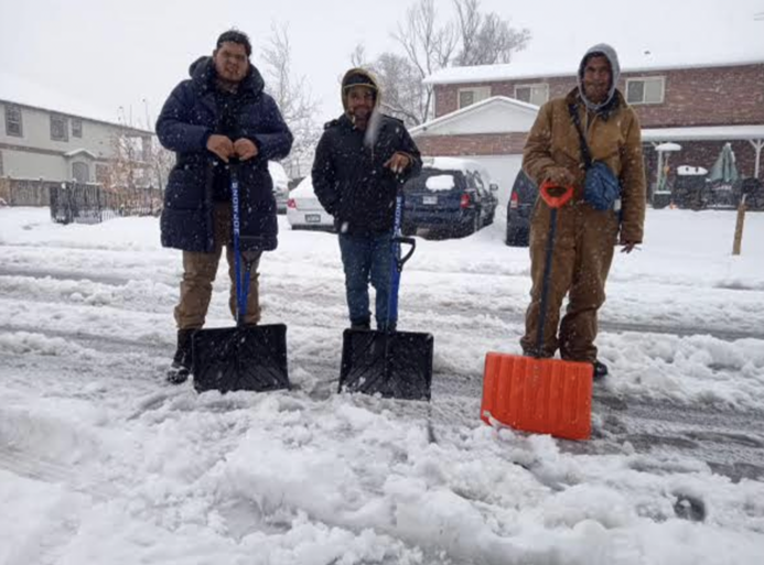 Migrants stand outside with shovels in the snow in Denver