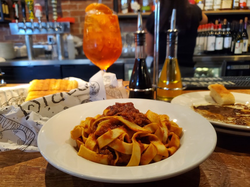 a bowl of pasta with red sauce in front of an Aperol spritz