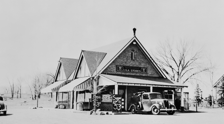 a black and white photo of a small building with an old car in front