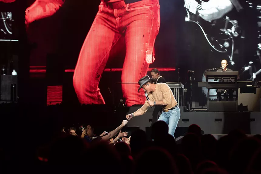 man holding a microphone in a cowboy hat reaching out to an audience member
