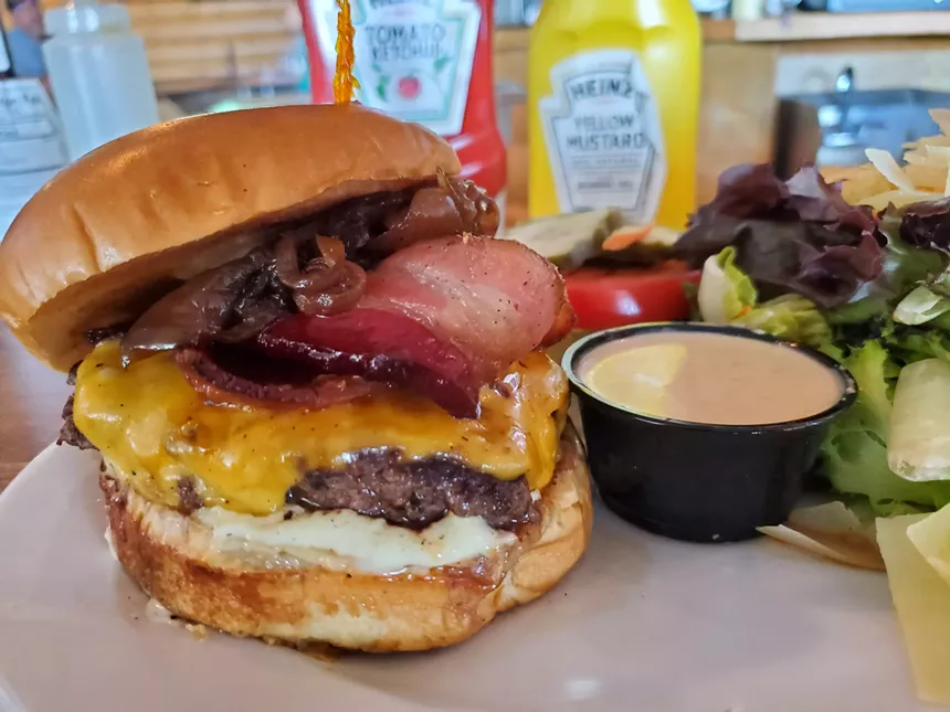 a bacon cheeseburger in front of bottles of ketchup and mustard