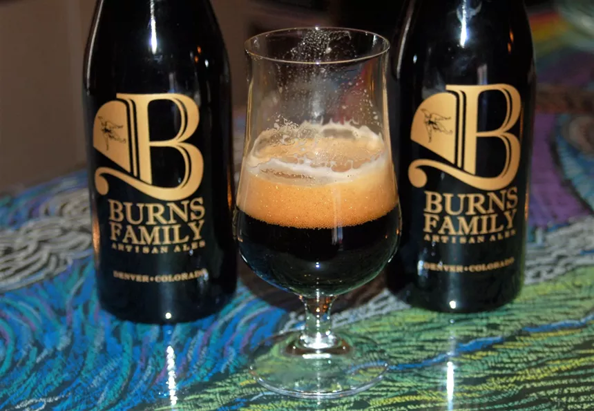 dark beer in a glass in front of two bottles of beer
