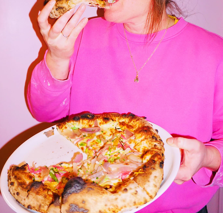 person in a pink sweatshirt holding a pizza and eating a slice