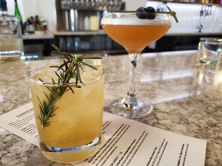 a cocktail with a sprig of rosemary in front of another garnished with blueberries