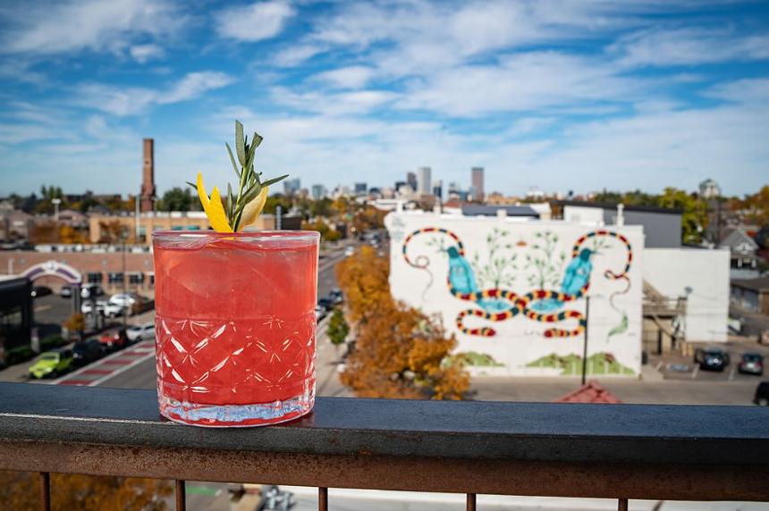a pink cocktail in a glass on a railing with a city view behind it