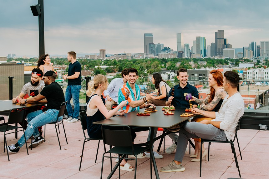smiling people sitting at an outdoor table on a rooftop with food and drink