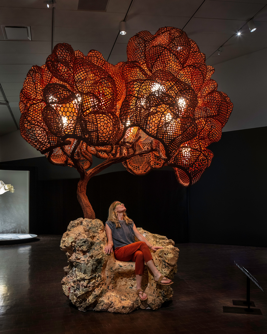 person sitting in a sculptural chair like a tree