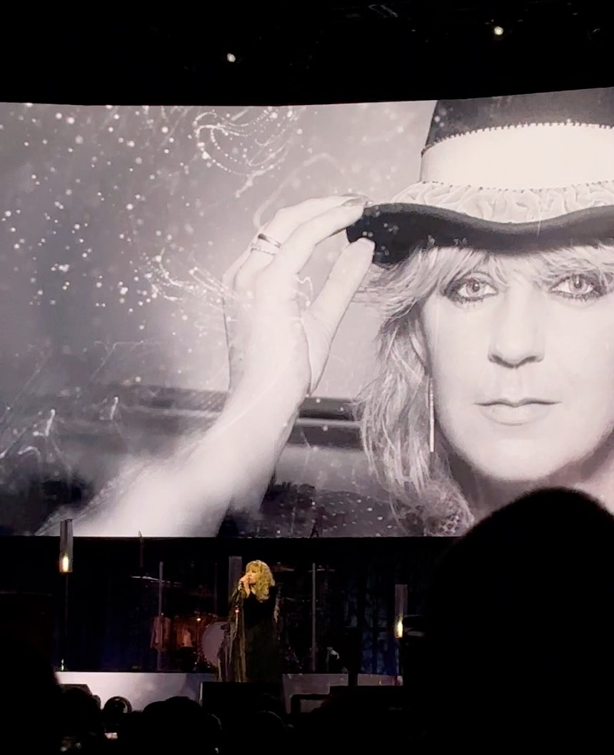 stevie nicks performing on stage with a photo of christine mcvie in the background