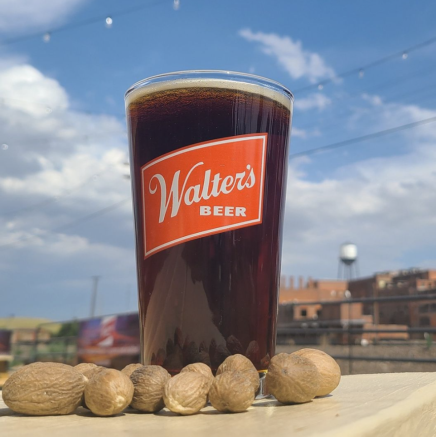 Brown beer in a pint glass with nutmegs in the foreground.