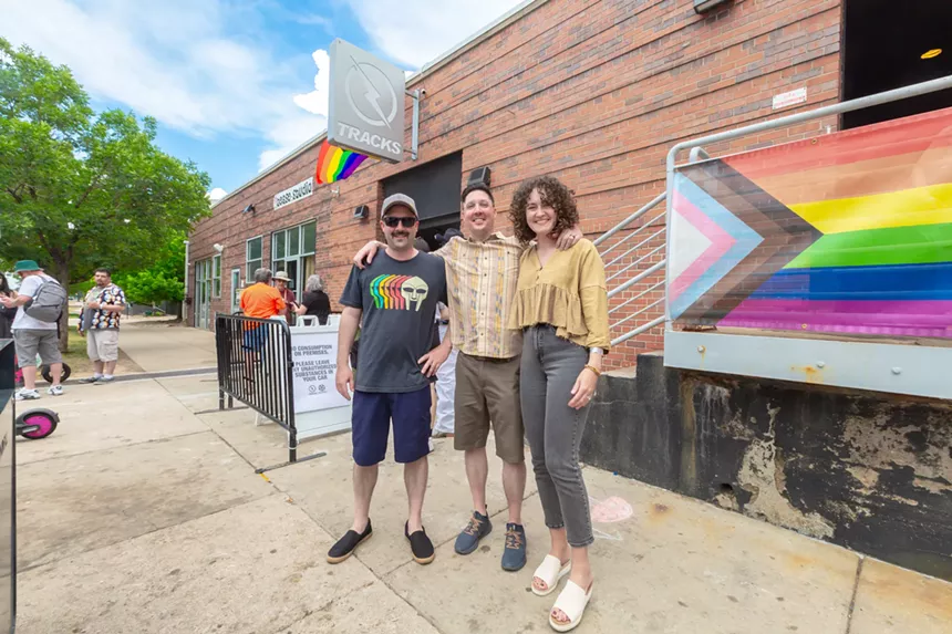 Friends stand outside next to Pride flag