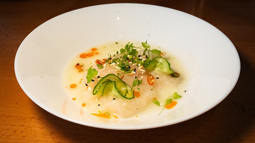 scallop crudo in a white bowl topped with cucumber slices