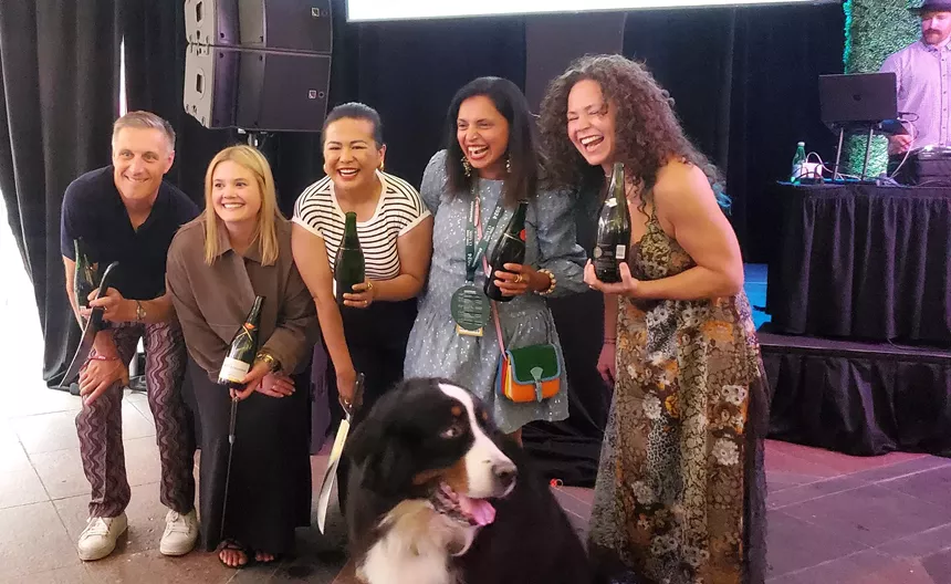 five people posing and holding bottles of wine