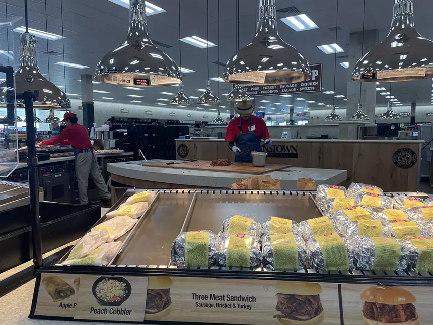 a person working behind a counter stocked with wrapped sandwiches