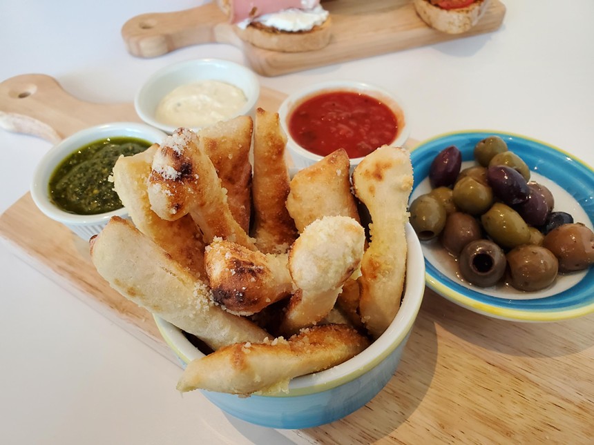 a small bowl of breadsticks next to a small bowl of olives