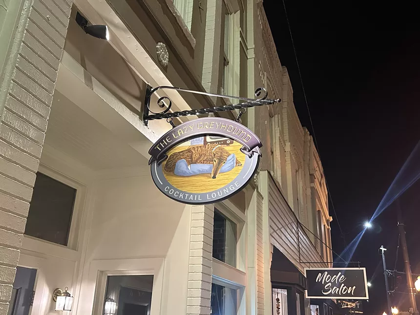 an oval sign that says "the lazy greyhound cocktail lounge"