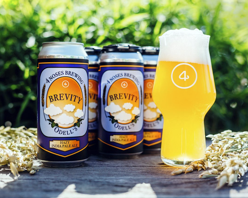 Bright yellow cloudy beer next to cans outside.