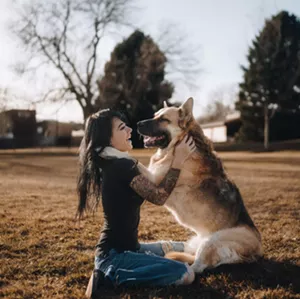 A woman embraces a German Shepherd dog in a field of grass.