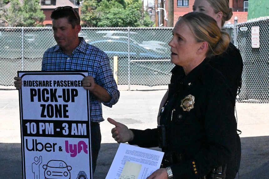 A woman talks while a man holds a sign.