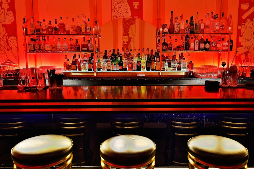 three barstools in front of a bar bathed in red light