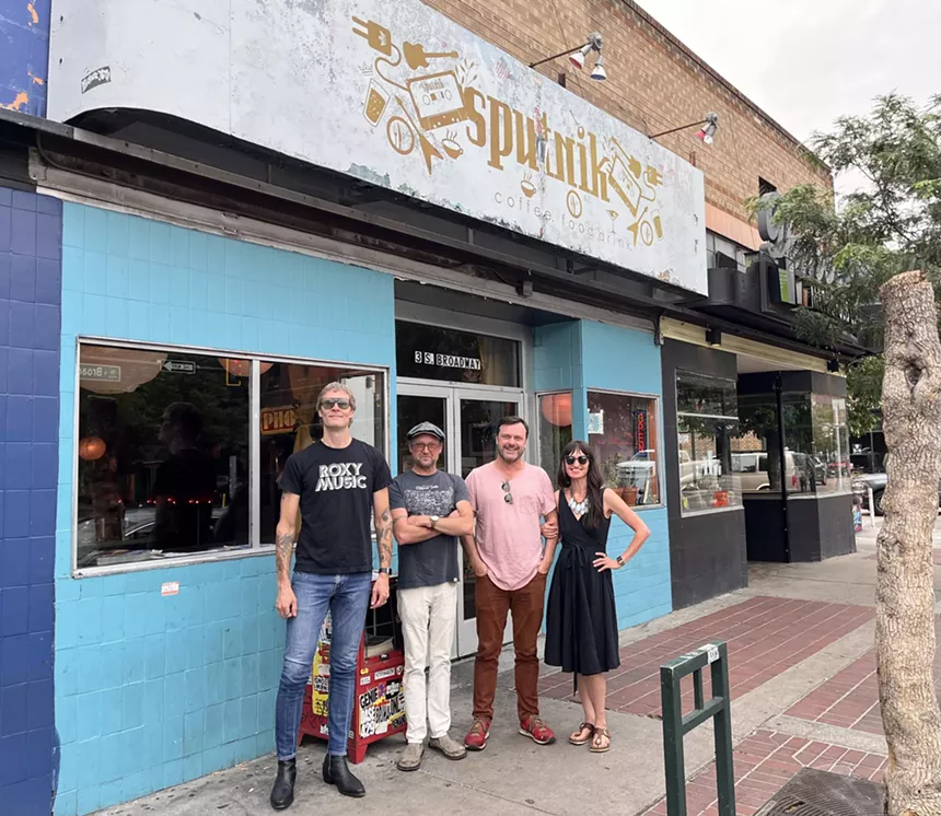 four people posing outside a light blue building