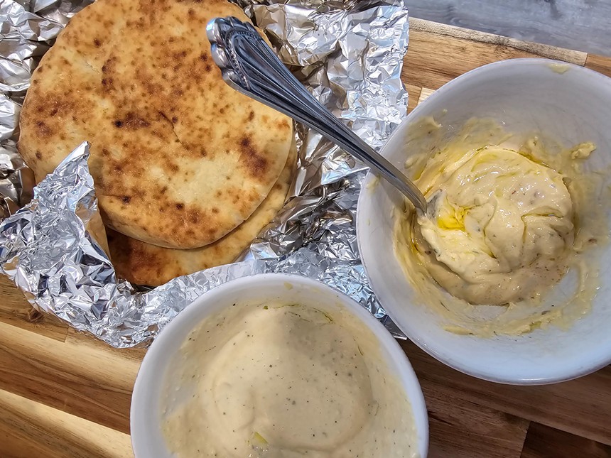 pita wrapped in foil next to two bowls of hummus