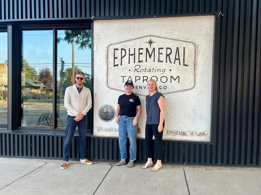 two woman and man in front of sign.