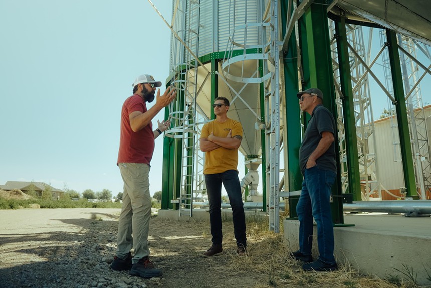 Three men talking in front of a grain silo.