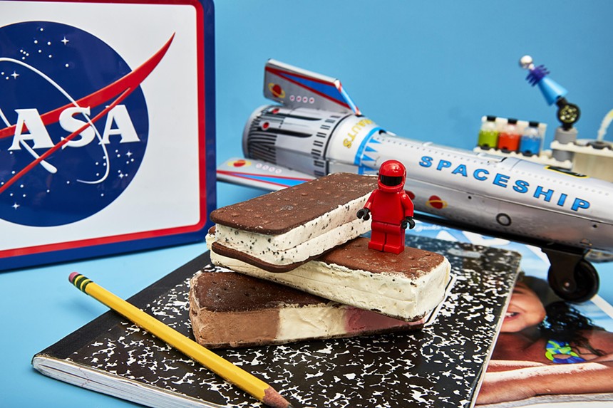 A stack of Astronaut Foods ice cream sandwiches alongside a NASA lunchbox and toy rocket ship