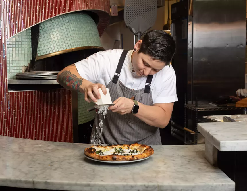 person in an apron grating cheese onto a pizza
