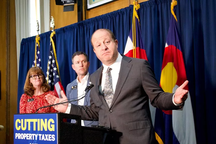 Colorado governor in front of flags