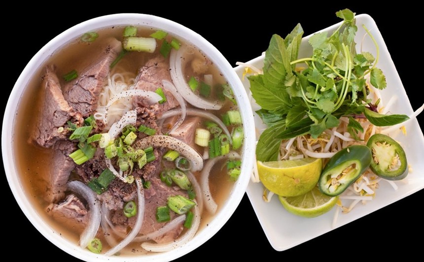 A bowl of pho next to a plate of herbs