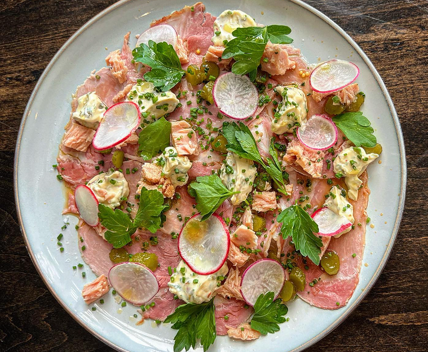 sliced pork on a white plate garnished with sliced radishes