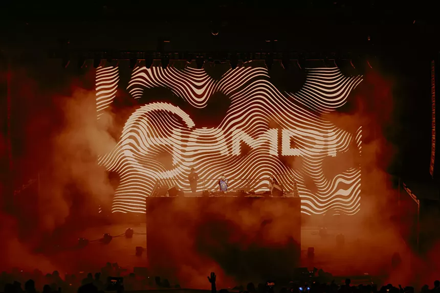 A photo of Hamdi performing behind a large stage highrise with his name in the background.