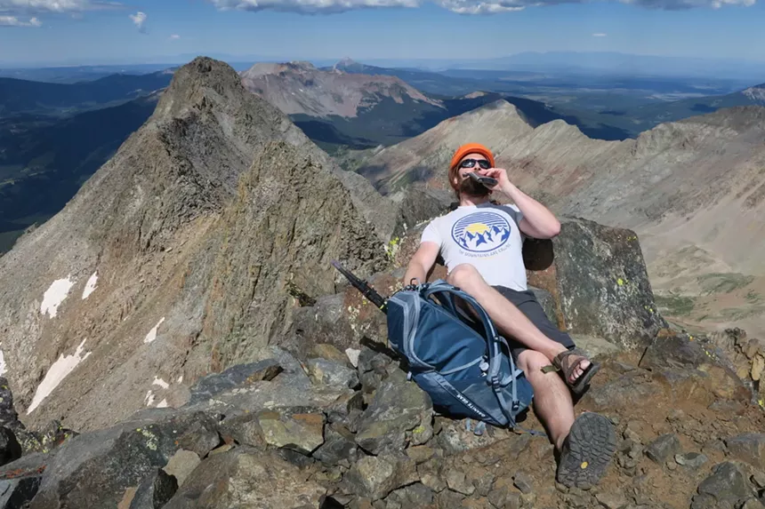 Chris Meehan wearing Chacos and drinking from a flask on a 14er peak